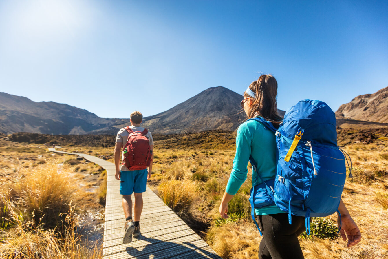New Zealand Hiking Couple Backpackers Tramping At Tongariro National Park. Male And Female Hikers Hiking By Mount Ngauruhoe. People Living Healthy Active Lifestyle Outdoors